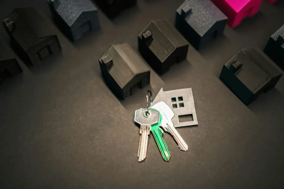 Nøkler med husformet nøkkelring blant rekker av små svarte modellhus
