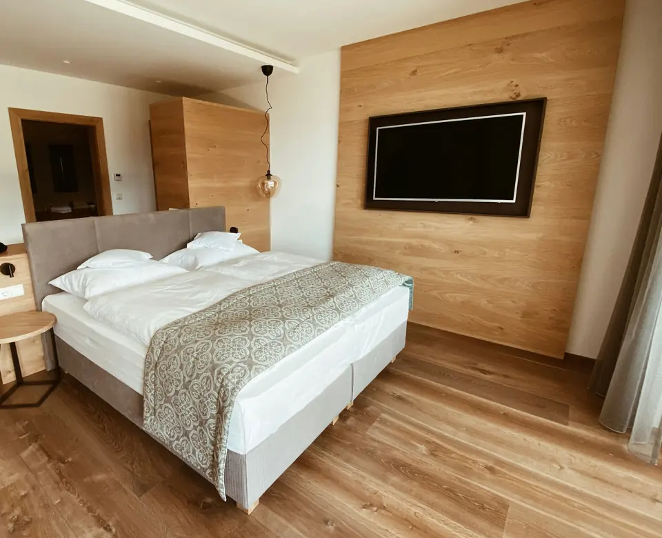 Hotellrom med dobbeltseng, eikepanel på veggen og en stor tv-skjerm
